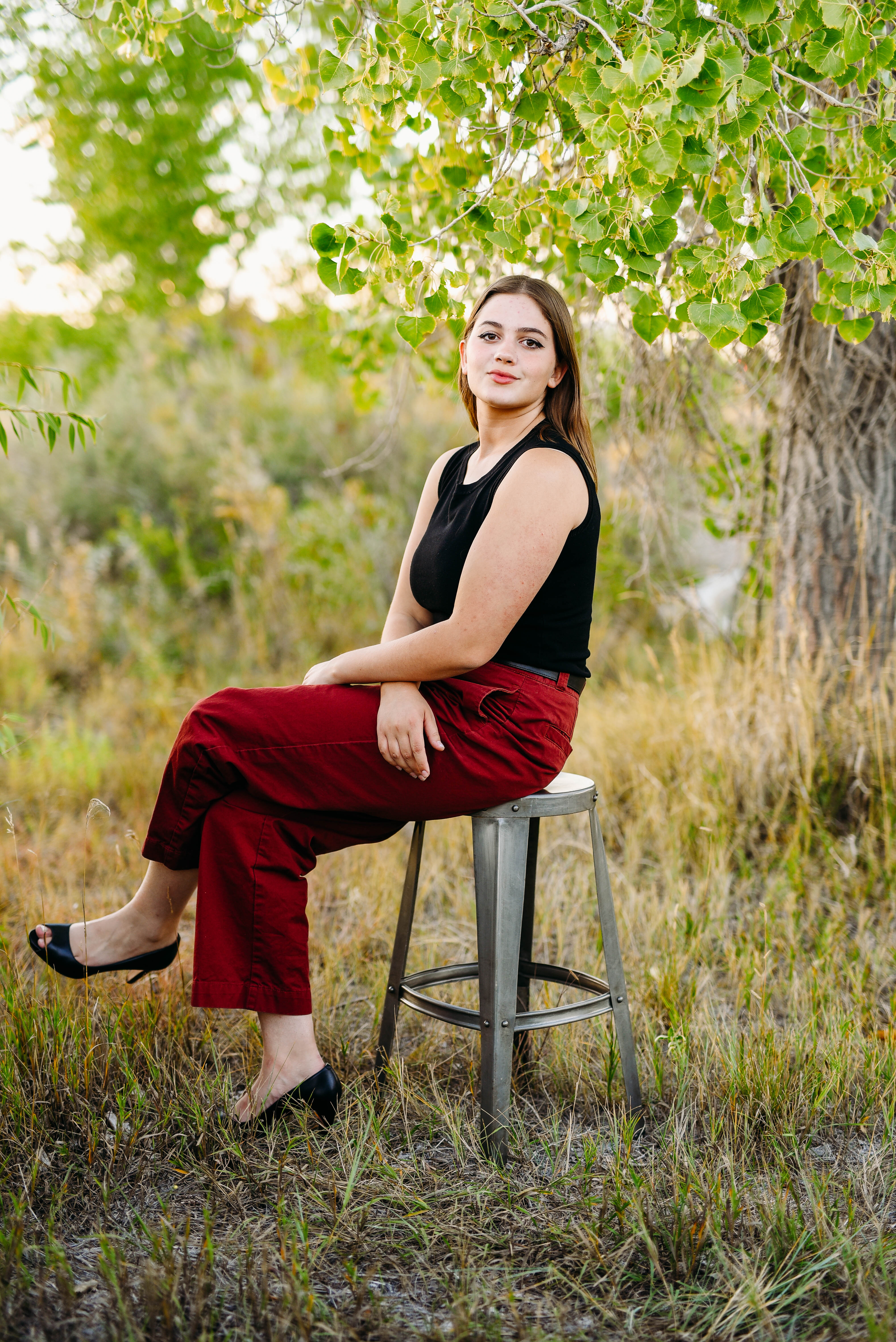 a senior girl is photographed sitting on a stool wearing red pants a black shirt