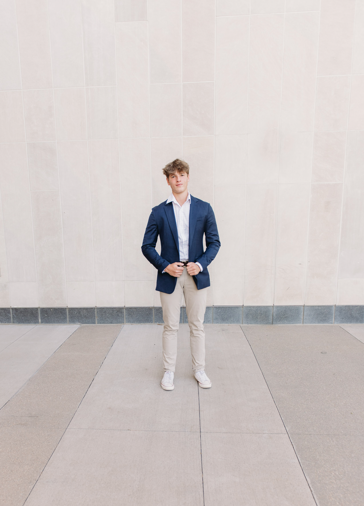 a senior boy dressed in a blue suit poses against a white wall