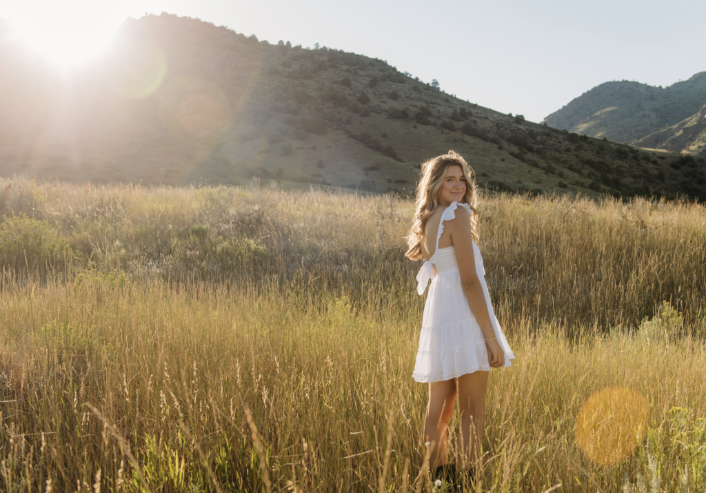 a senior girl poses in a field during golden hour