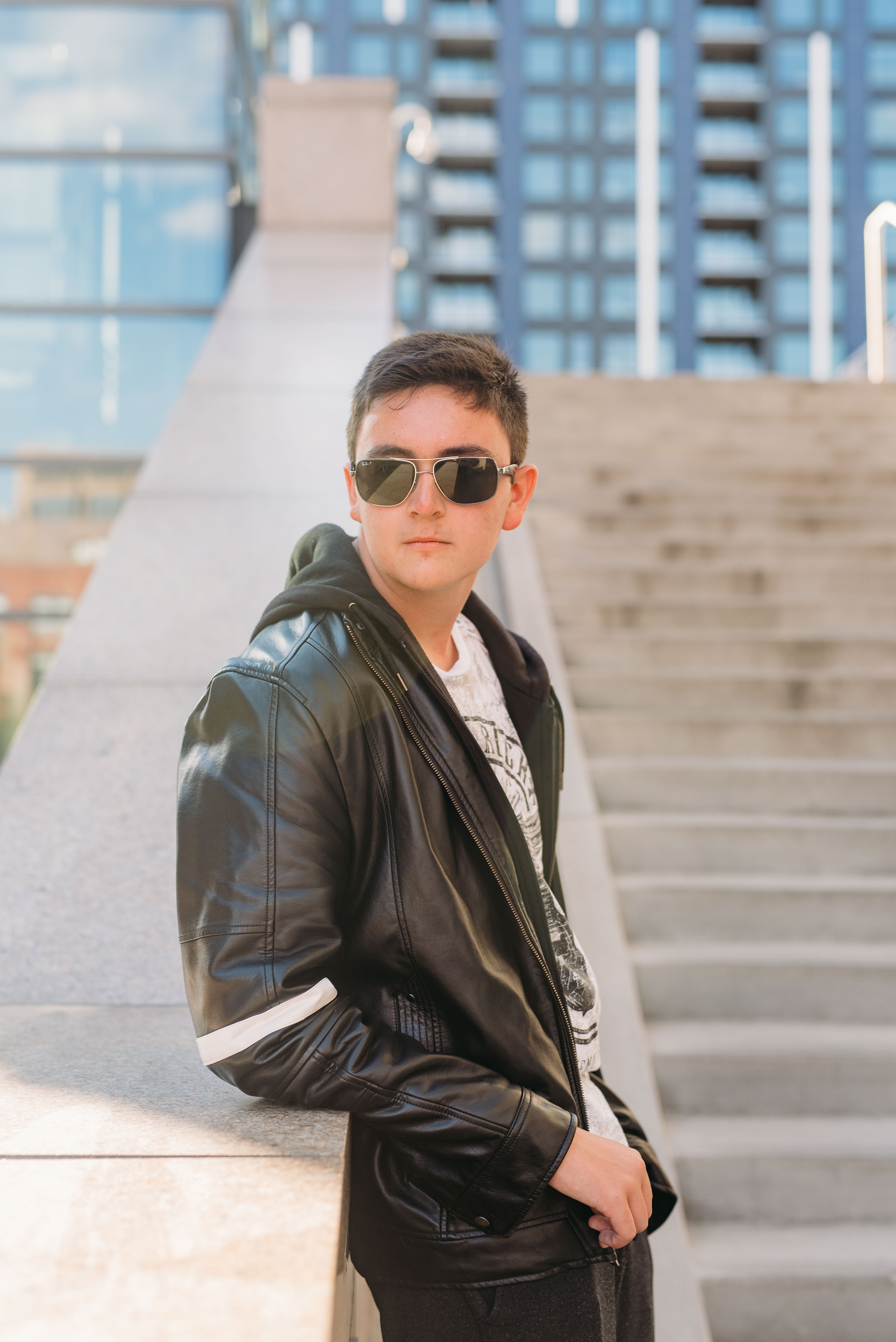 a boy rests on steps while wearing a black jacket and sunglasses